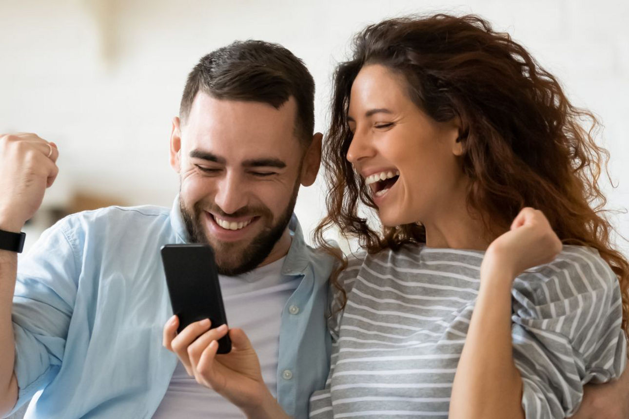 Mann und Frau schauen in ihr Handy und freuen sich