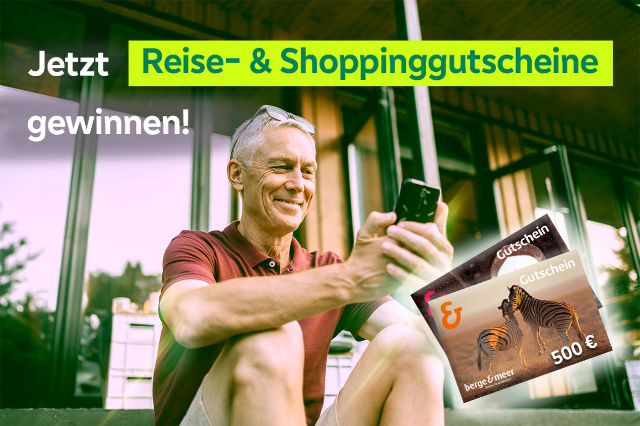 Mann sitzt lächelnd auf dem Boden und schaut auf sein Smartphone.