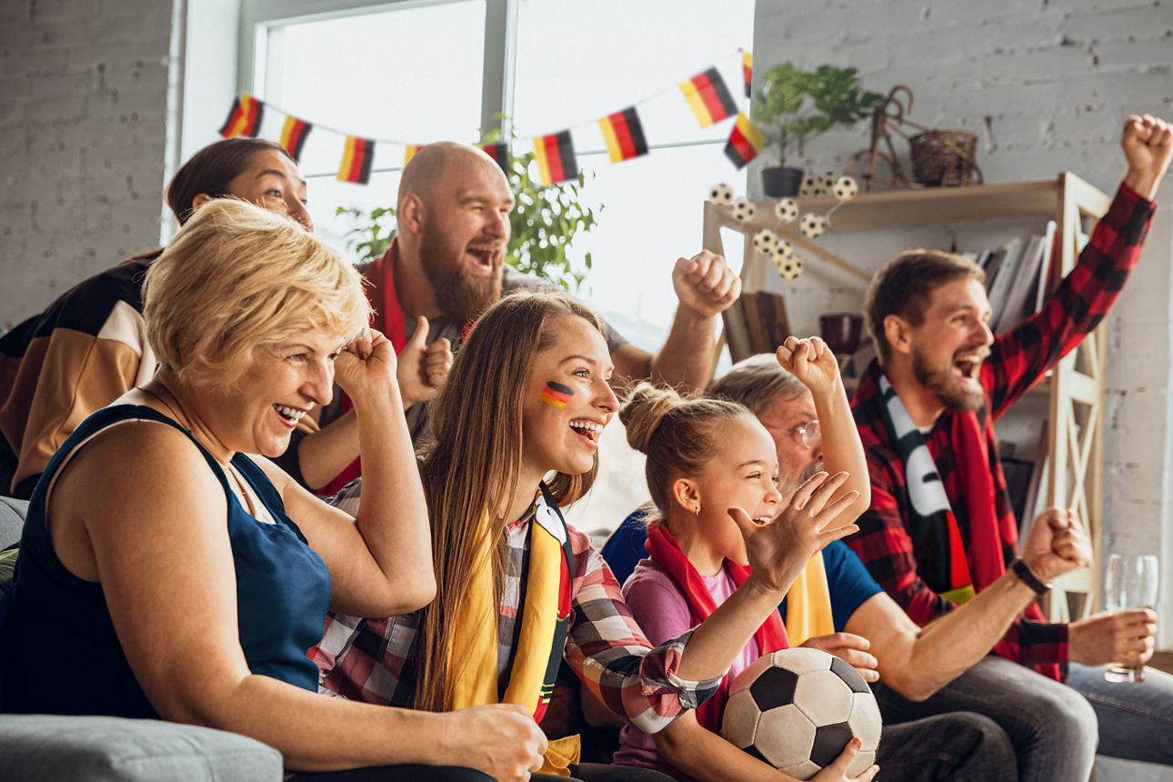 Aufgeregte, glückliche Familie schaut ein Fußballspiel zu Hause auf der Couch und jubelt.