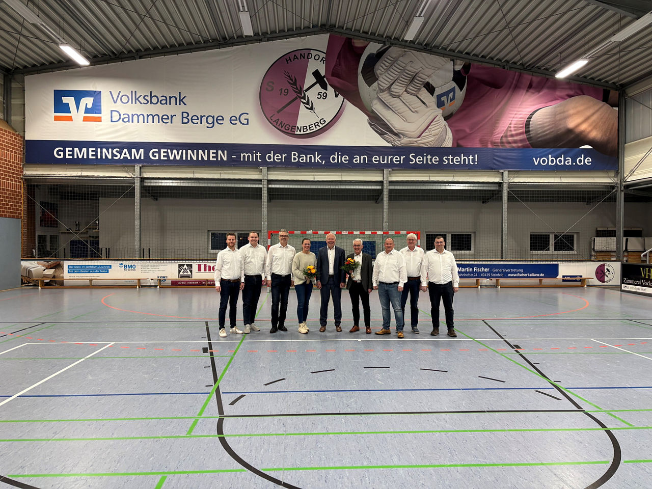 Mehrere Personen haben sich zum Foto in der Mitte einer Sporthalle aufgestellt