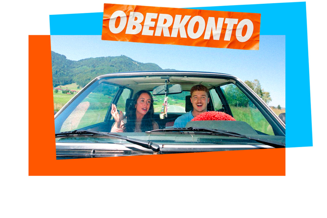 Eine Frau und ein Mann fahren im Auto und durch eine Berglandschaft. Darüber ein Sticker mit der Aufschrift "Oberkonto".