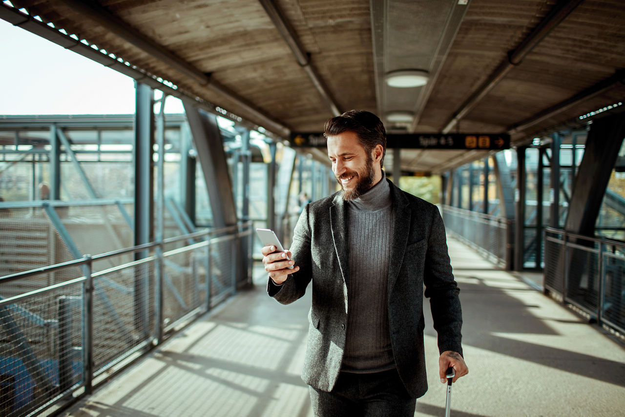 Ein Geschäftsmann am Bahnhof schaut lächelnd auf sein Handy