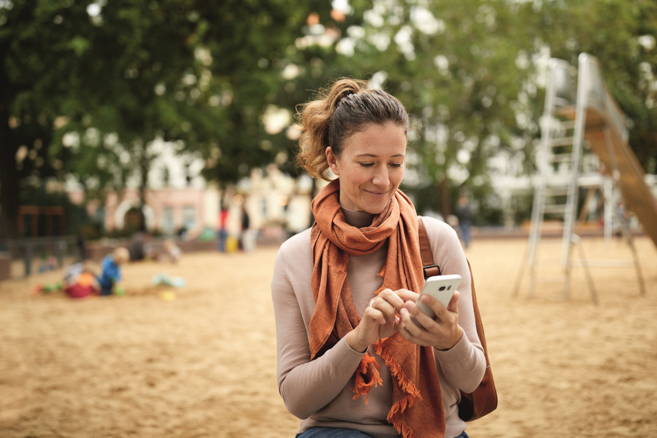 Frau prüft ihre Finanzen in der Banking App während sie auf einem Spielplatz ist.
