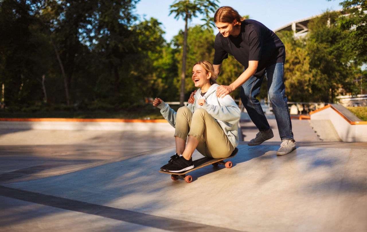Ein Junge schiebt ein Mädchen auf einem Skateboard und die beiden haben Spaß.