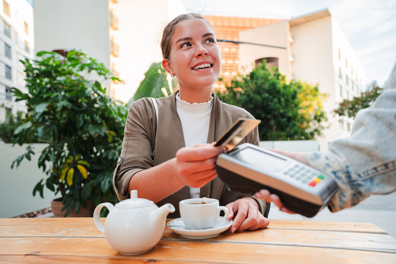 Eine junge Frau bezahlt in einem Kaffee kontaktlos.