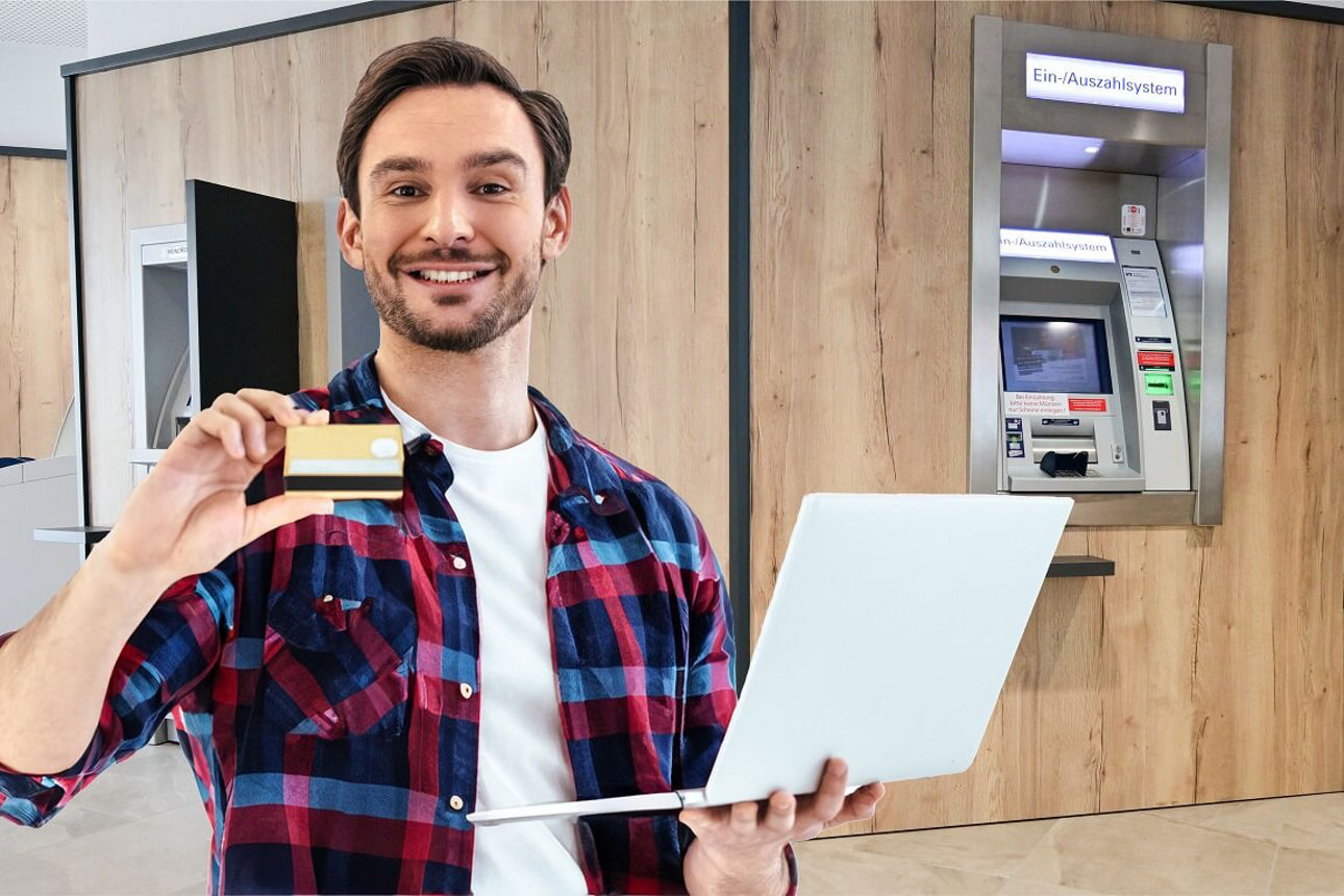 Kunde steht im SB-Raum einer Bank mit einer Kreditkarte und einem Laptop in der Hand 