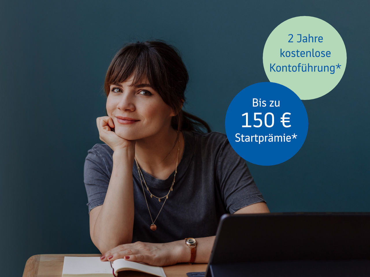 Frau sitzt lächelnd an einem Tisch vor einem Laptop.