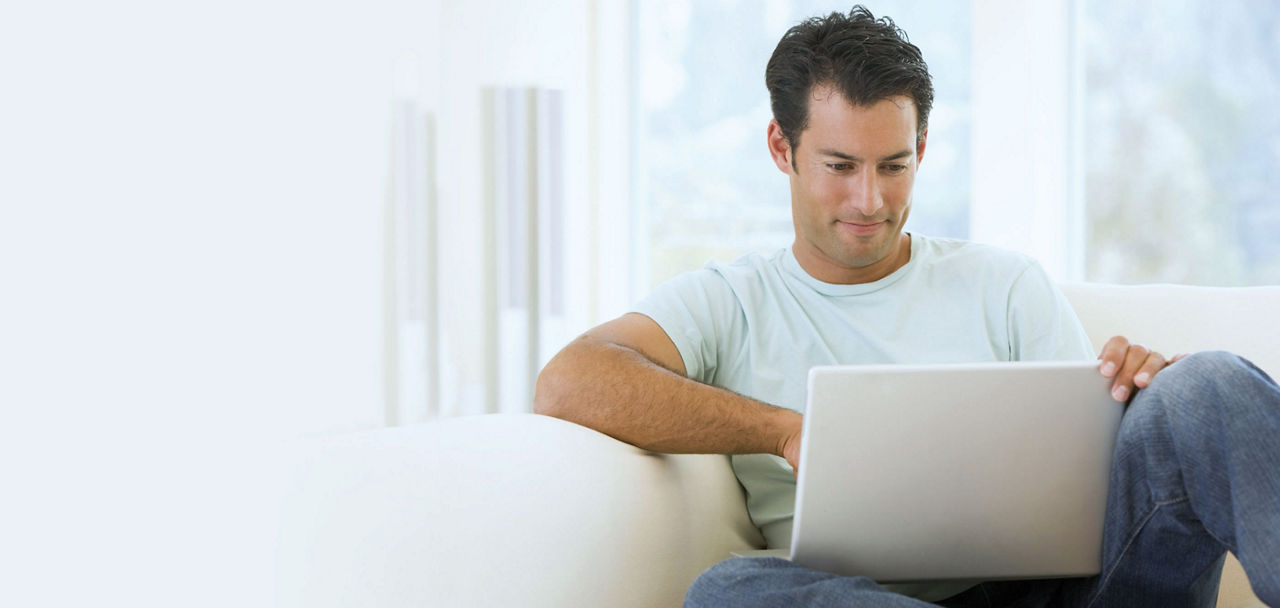 Mann sitzt mit Laptop auf dem Schoß auf einem Sofa