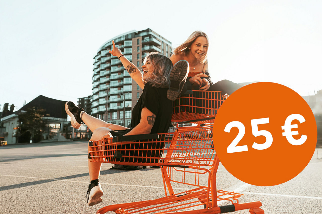 Zwei junge Frauen im Einkaufswagen lachen. Störer auf dem Bild mit 25 € Guthaben fürs erste Girokonto.