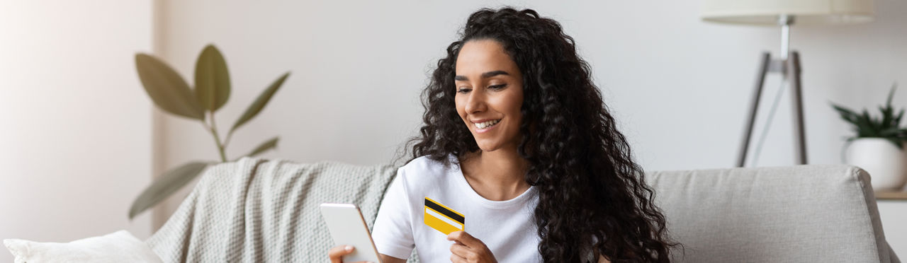 Junge Frau mit Girocard und Smartphone auf dem Sofa