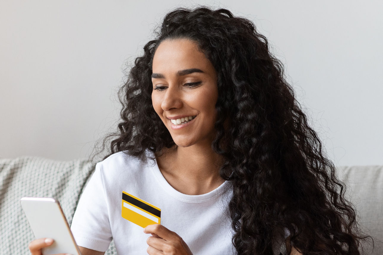Junge Frau mit Girocard und Smartphone auf dem Sofa