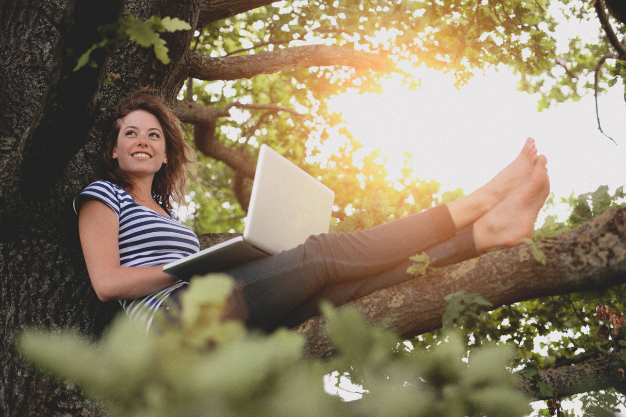 Junge Frau mit Laptop sitzt auf einem Baum