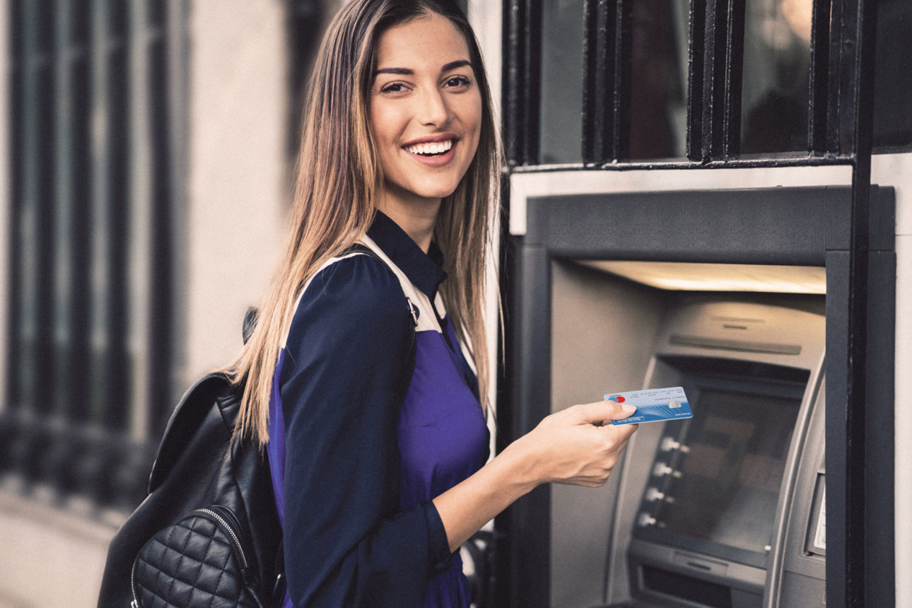 Junge Frau steht mit Karte vor Geldautomat