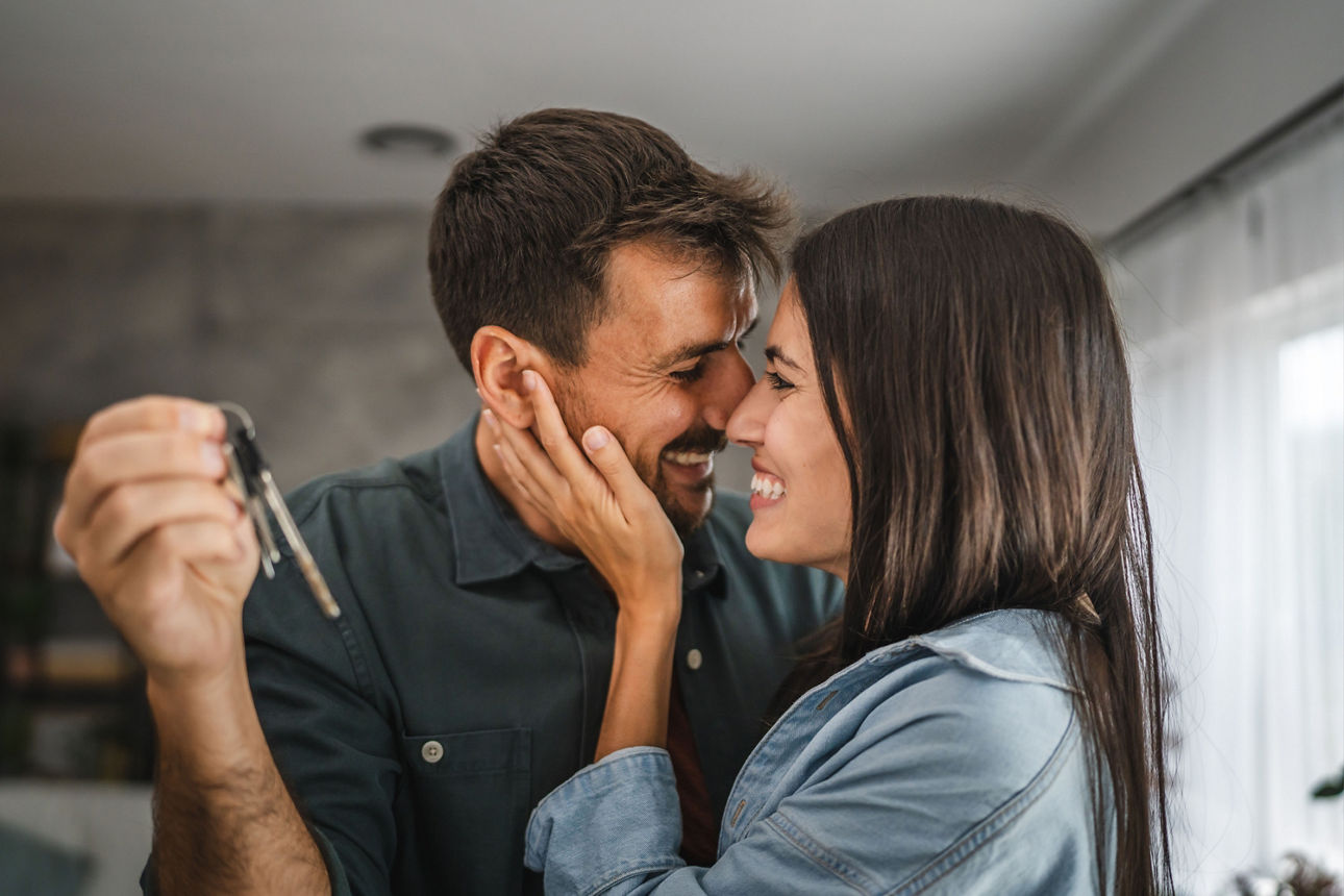 Glückliches Paar umarmt sich und der Mann hält einen Hausschlüssel in der Hand