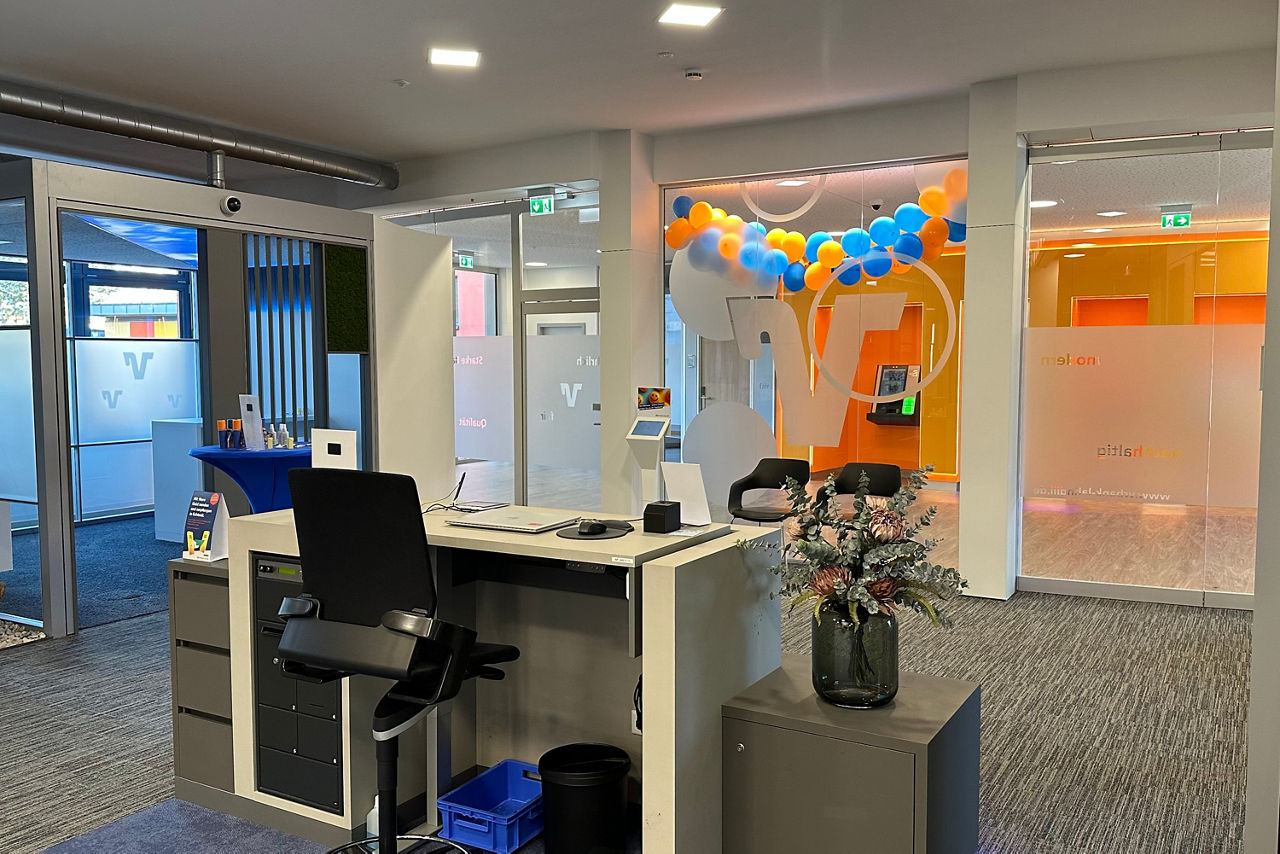 Moderner Empfangsbereich mit Schreibtisch, Bürostuhl, Glasvase mit Blumen und blauen sowie orangen Luftballons an der Wand