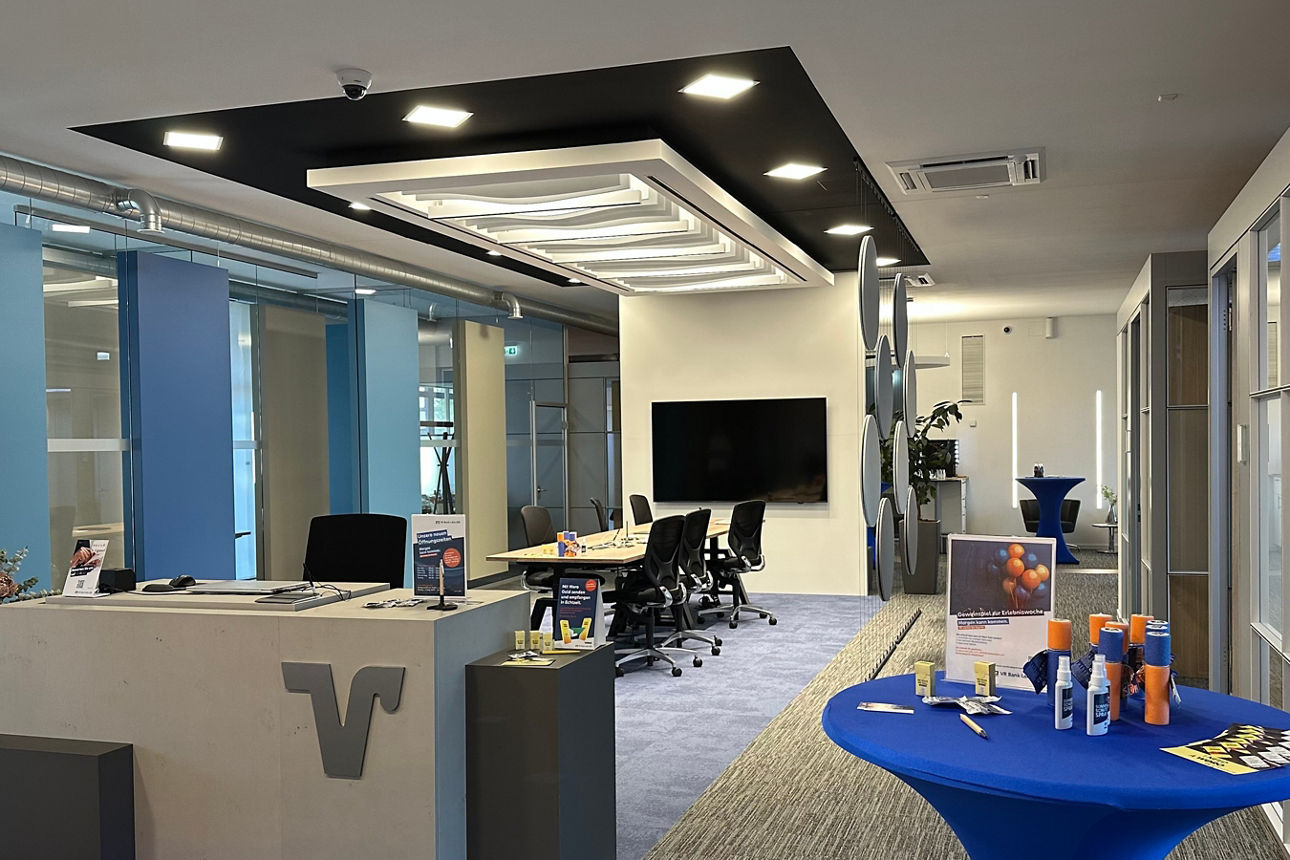 Moderner Empfangsbereich mit Tresen, mehreren Stühlen, blau gedecktem Stehtisch und großem Bildschirm an der Wand