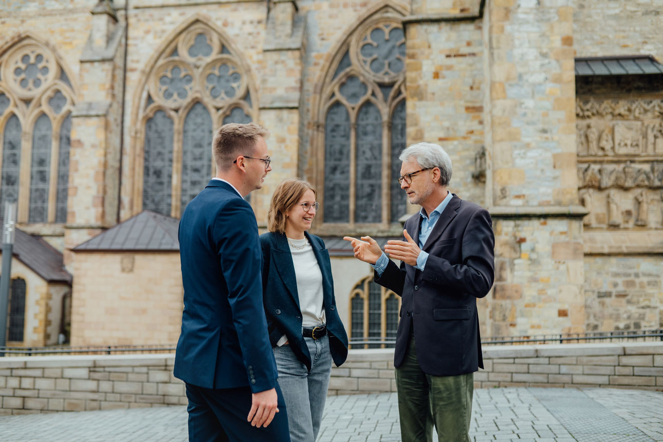 Drei Mitarbeitende stehen vor dem Paderborner Dom und unterhalten sich