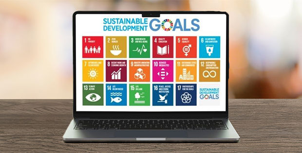 Auf einem Holztisch steht ein Laptop, auf dem die Ziele für nachhaltige Entwicklung (SDGs) abgebildet sind. 