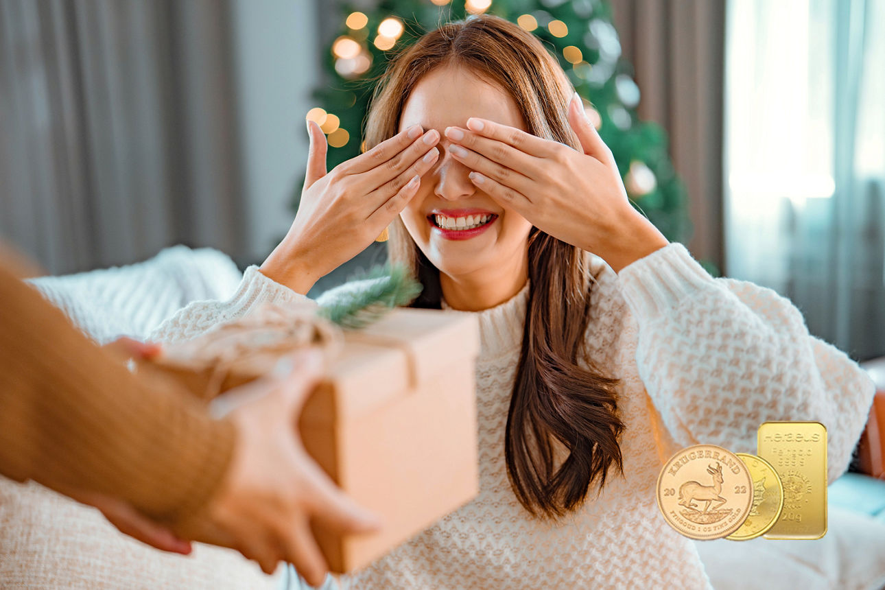 Frau hält Augen vor einem Weihnachtsbaum zu, ihr wird ein Geschenk hingehalten, Goldmünzen sind zu sehen