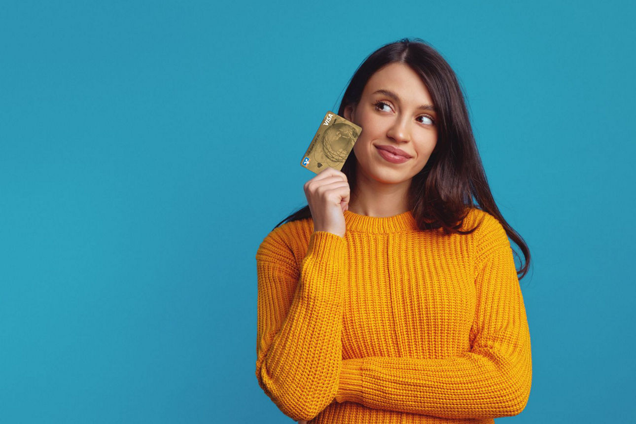 Person vor blauem Hintergrund hält eine goldene Kreditkarte und trägt einen orangefarbenen Strickpullover