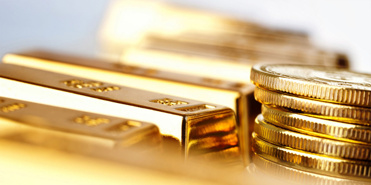 Mehrere glänzende Goldbarren und einen Stapel Goldmünzen in Nahaufnahme mit einer warmen, goldfarbenen Lichtreflexion sind abgebildet
