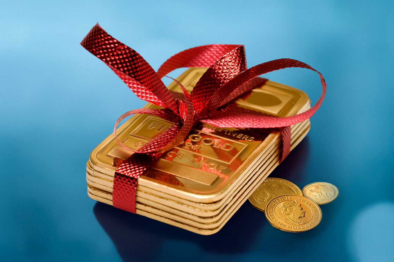 Goldbarren mit roter Schleife und Münzen vor festlich-blauem Hintergrund