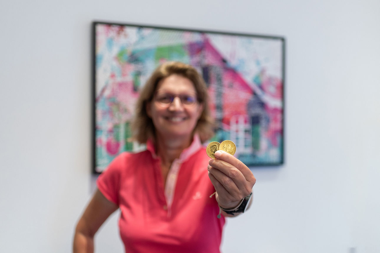 Zwei Goldmünzen werden in die Kamera gehalten. Der Hintergrund mit einer Frau ist unscharf.