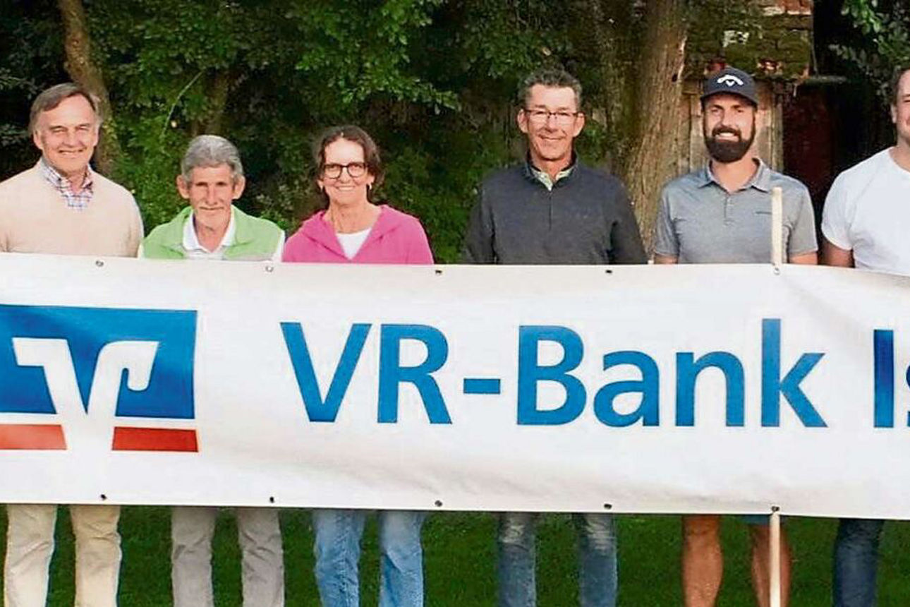 Neun Menschen lächeln in die Kamera, dabei stehen sie hinter einem langen Banner der VR-Bank Isar-Vils eG.
