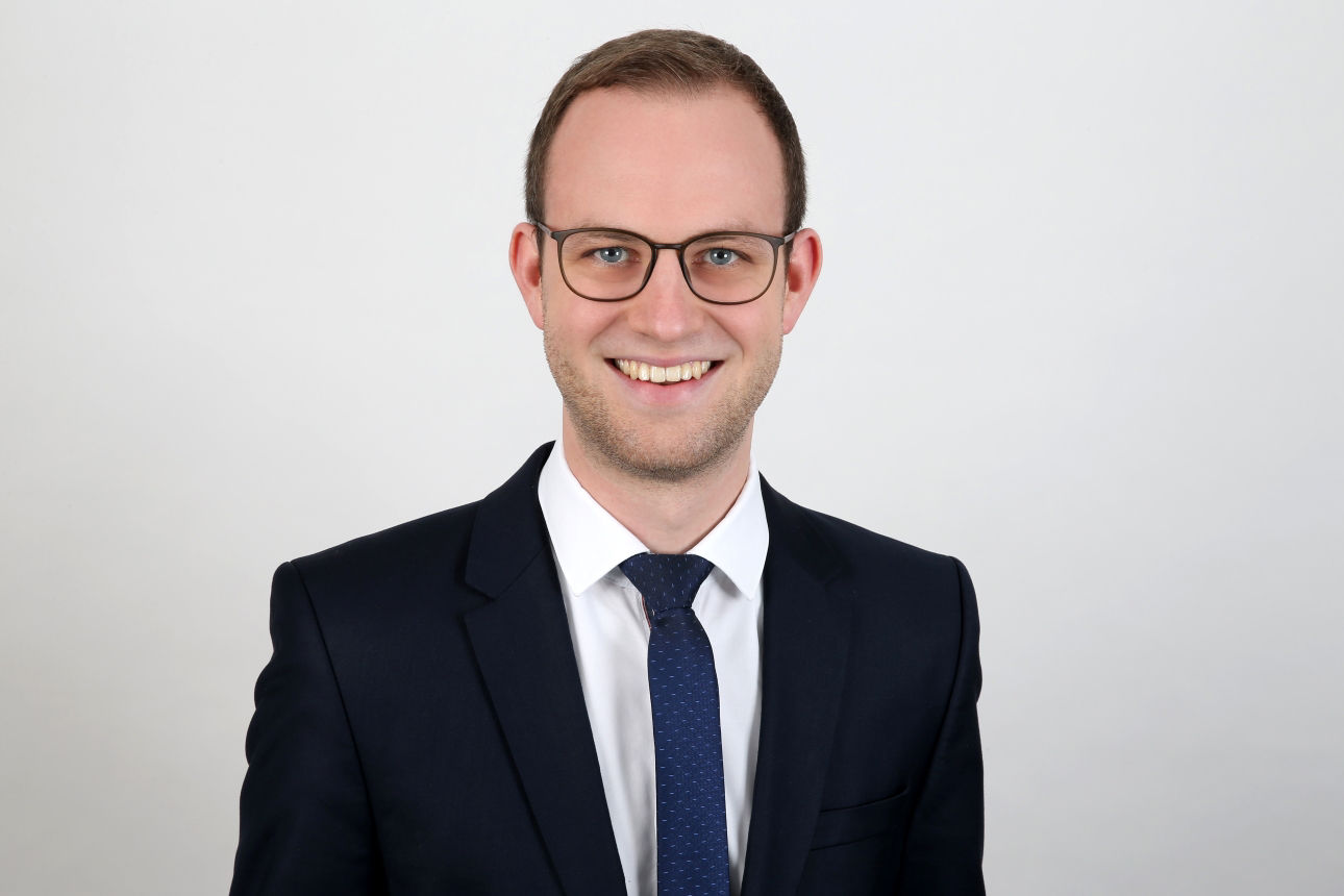 Ein lächelnder Mann in einem Anzug schaut in die Kamera.