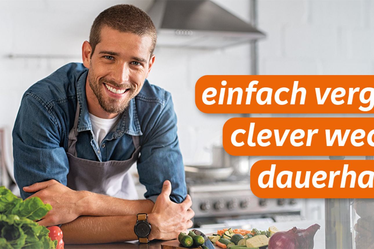 Junger Mann steht in seiner Küche und lächelt in die Kamera