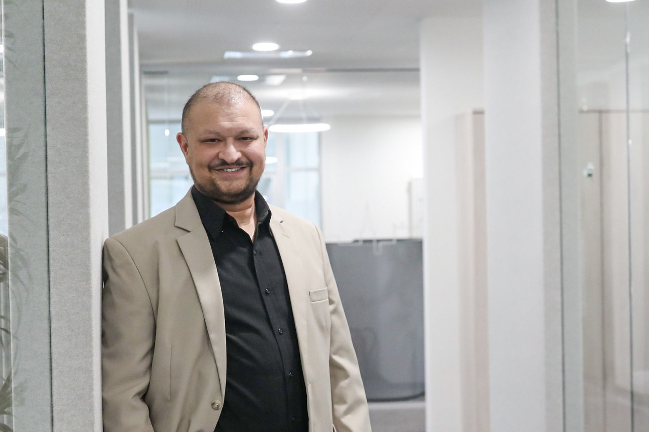 Mann steht im Gang angelehnt an die Wand und lächelt in die Kamera