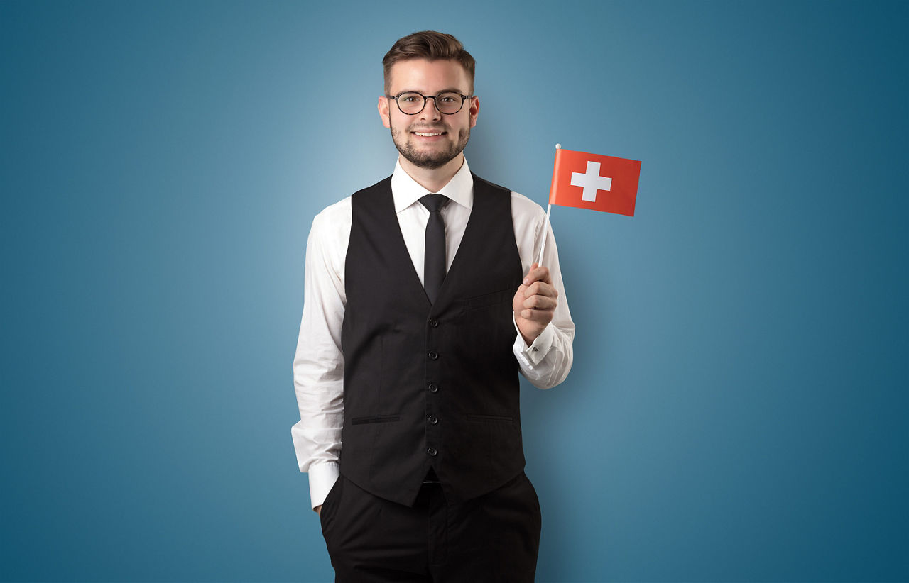 Ein Mann mit einer Schweizer Flagge in der Hand vor einem blauen Hintergrund.