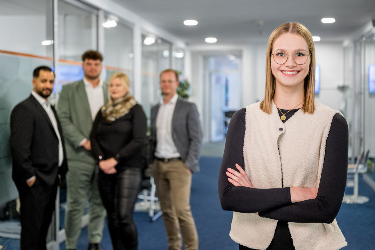 Eine Kollegin steht im Vordergrund und vier Kolleginnen und Kollegen im Hintergrund. 