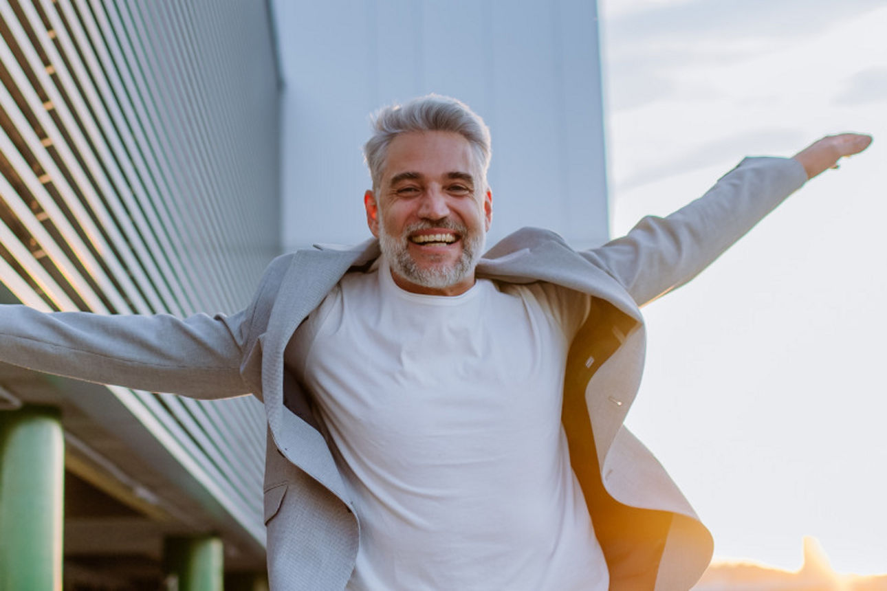 A portrait of happy energetic mature businessman with arms outstretched balancing on wall , feeling free, work life balance concept.