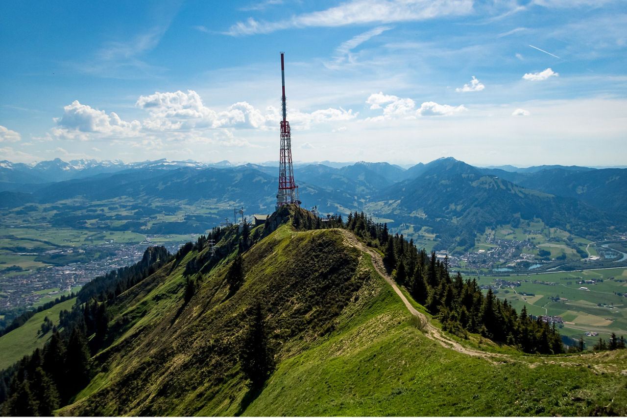Blick vom Grünten in das Allgäu mit Bergen im Hintergrund und blauem Himmel