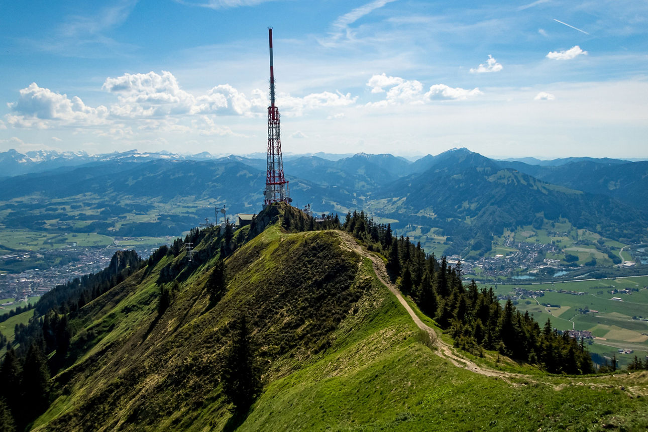 Blick vom Grünten in das Allgäu mit Bergen im Hintergrund und blauem Himmel