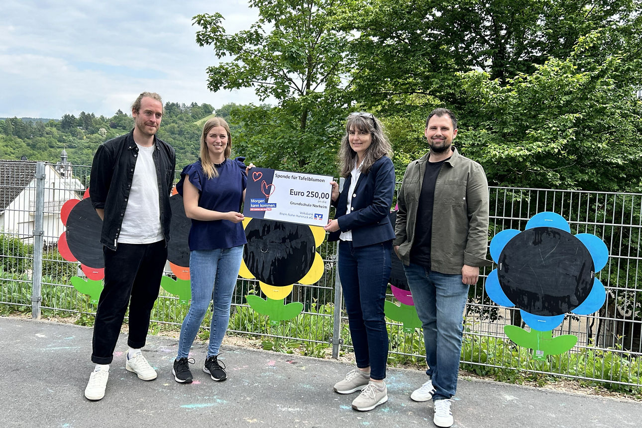 Vier Personen stehen vor einem Zaun, zwei halten einen Spendenscheck in der Hand.