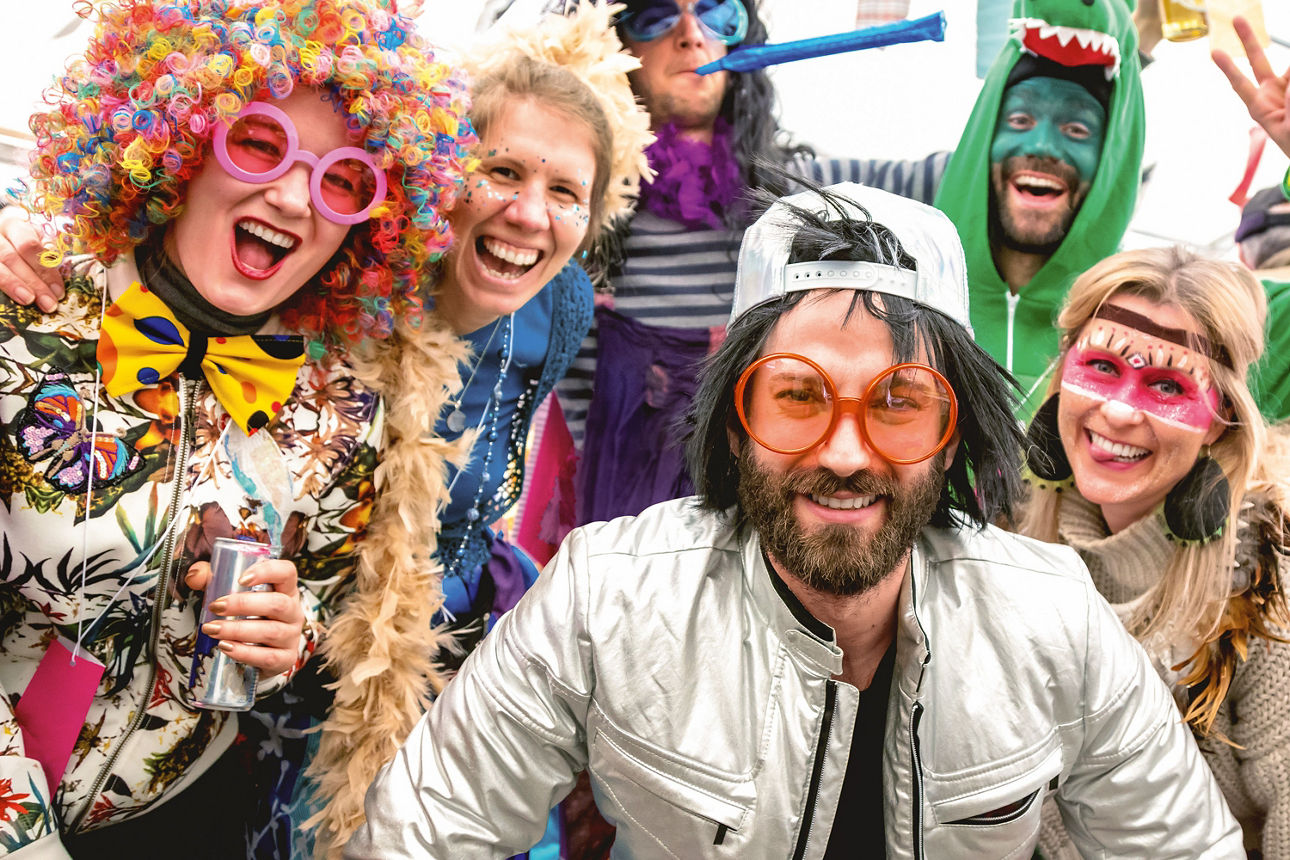 Sechs Personen tragen bunte Kostüme und Hüte, während sie gemeinsam lachen und Spaß haben. 