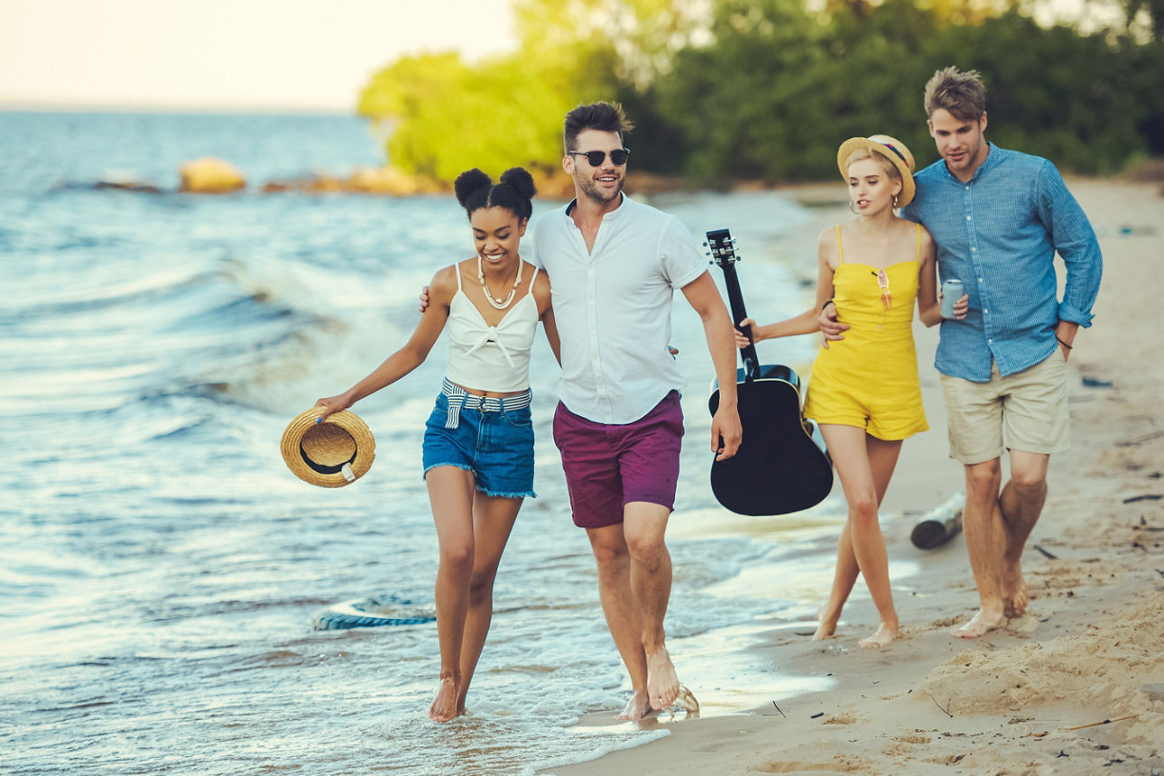 Vier Strandbesucher gehen zusammen und haben eine Gitarre dabei.  