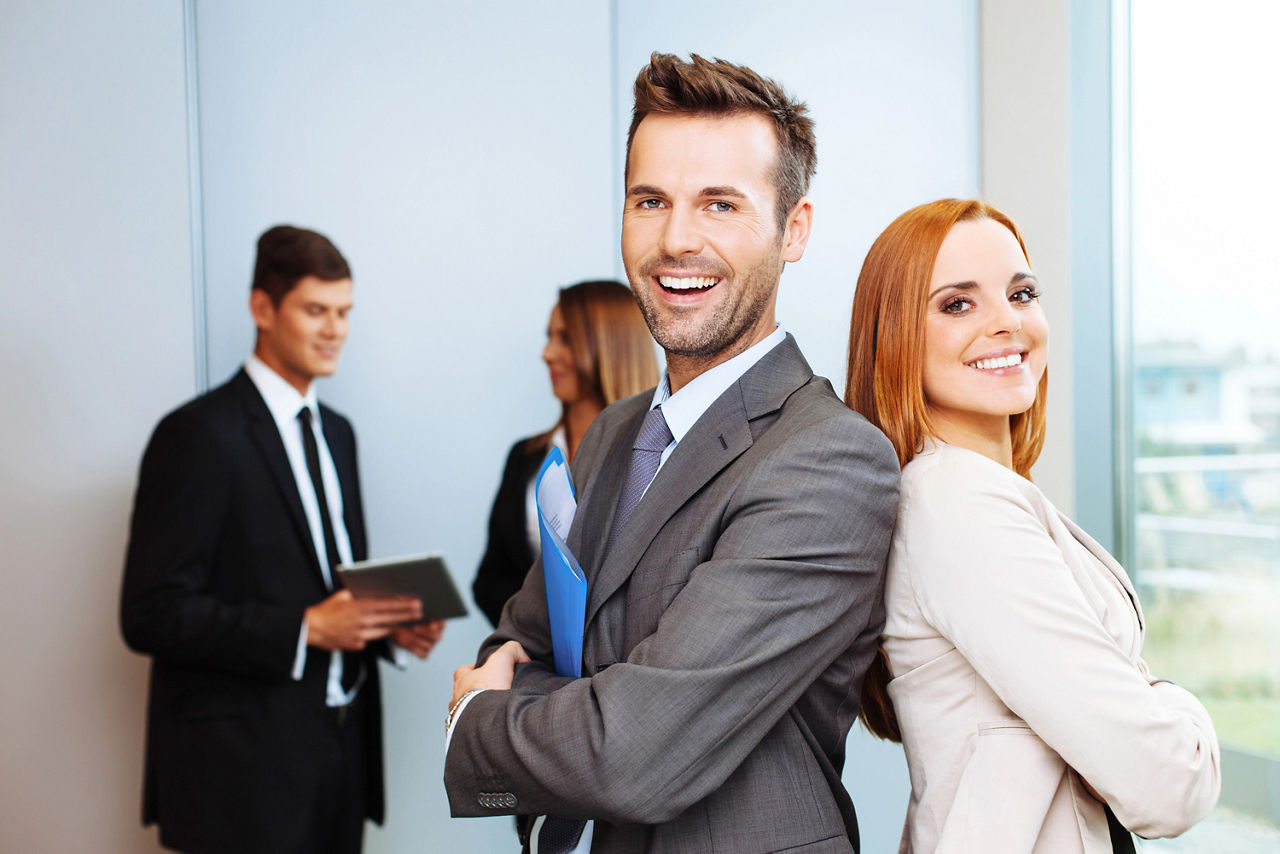 Frau mit lockigem, rotem Haar, lächelnd und mit Smartphone in der Hand, stehend in einer Stadtumgebung.