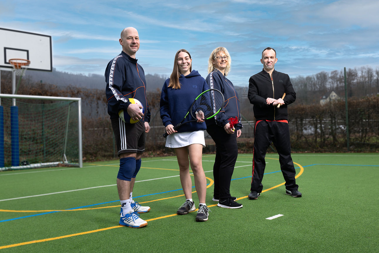 Vier Mitarbeitende im Sportoutfit stehen auf einem Sportplatz