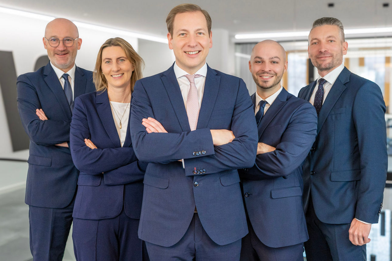 4 Männer und 1 Frau stehen lächelnd nebeneinander