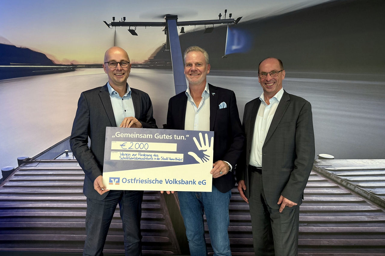 Guido Mülder, Martin Deymann und Georg Möller stehen vor einem maritimen Bild und halten den Spendenscheck