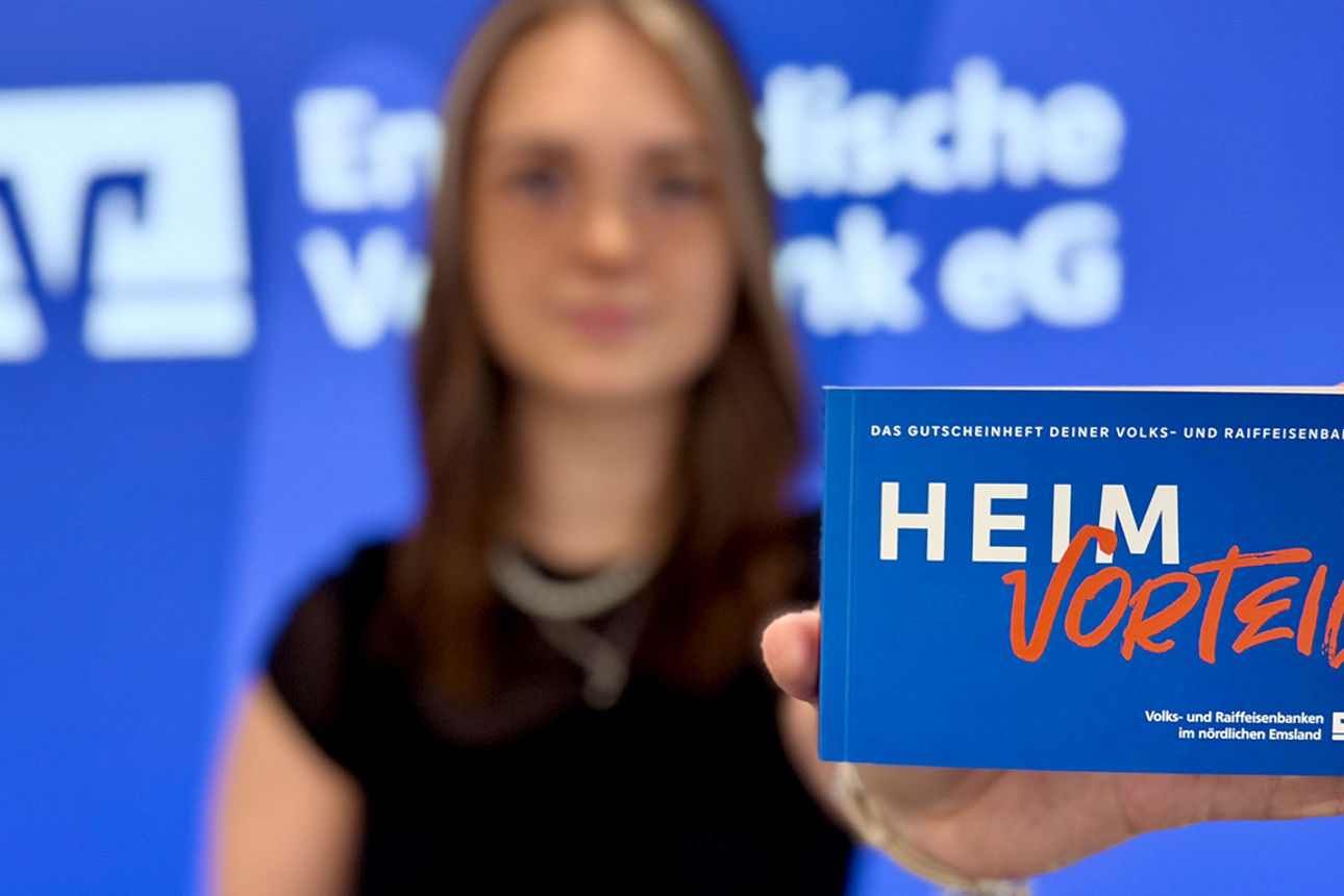Eine Mitarbeiterin hält vor unserer Pressewand das neue Gutscheinheft in den Vordergrund