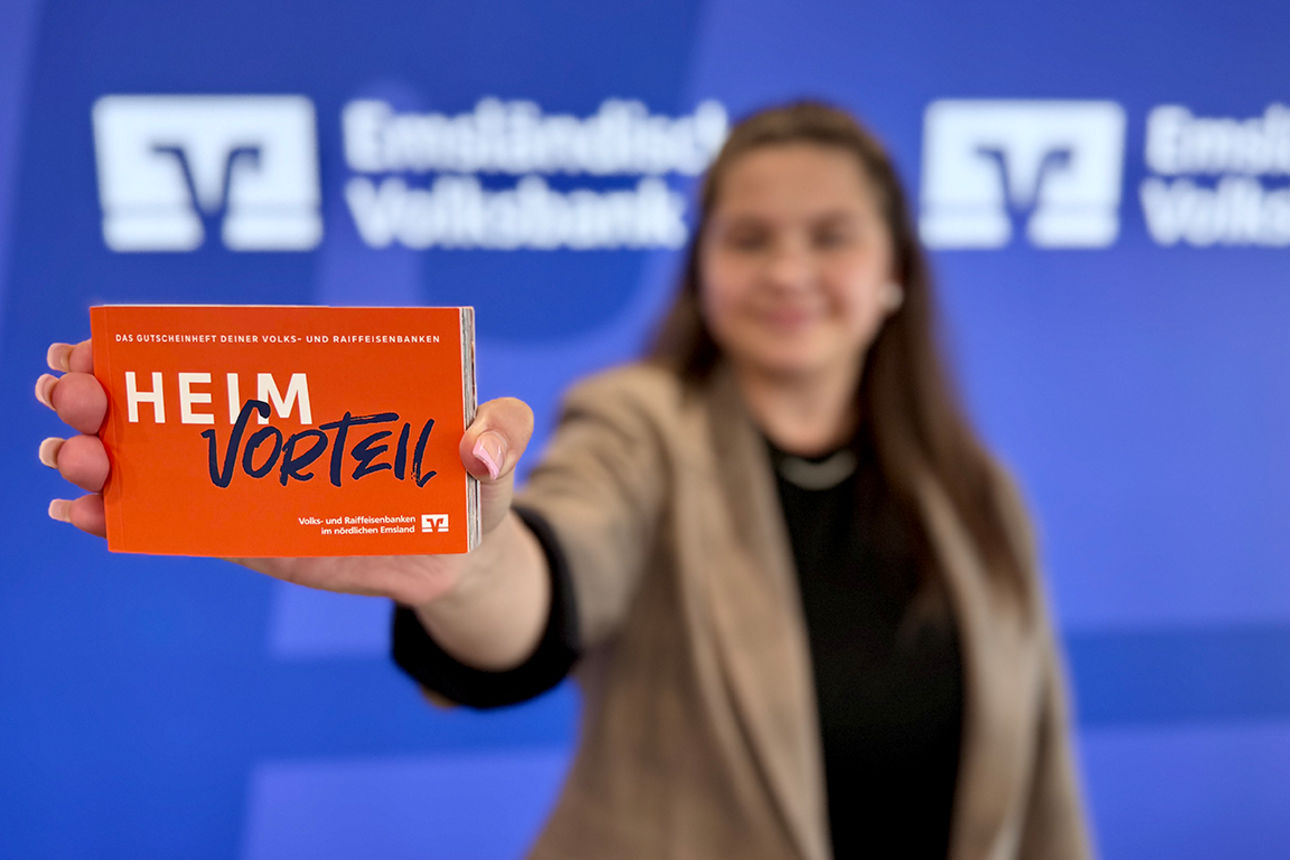 Eine Mitarbeiterin hält vor unserer Pressewand das neue Gutscheinheft in den Vordergrund