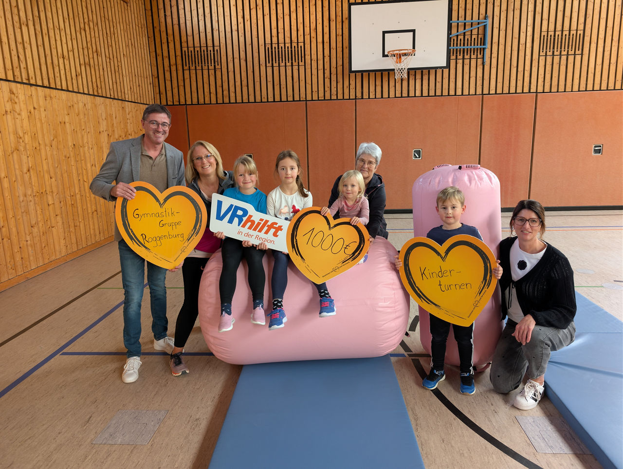 Gruppe in Turnhalle mit rosa Hüpfburg und Herzschildern, gemeinsames Spendenfoto