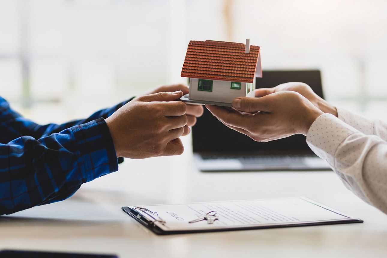 Zwei Personen halten ein kleines Miniaturhaus in den Händen