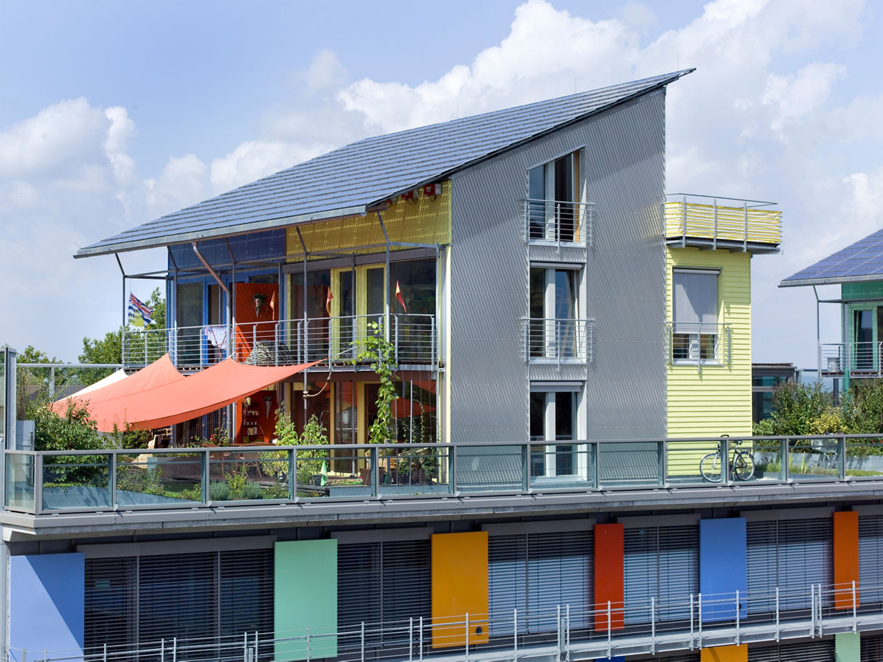 Ein modernes Wohngebäude mit bunter Fassade, Solarpanels auf dem Dach und großzügigem Balkonbereich.