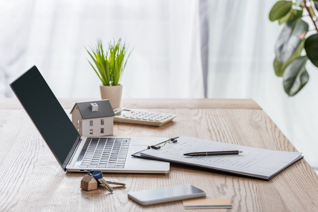 Laptop auf einem Holztisch inklusive Unterlagen und einem kleinem Holzhaus