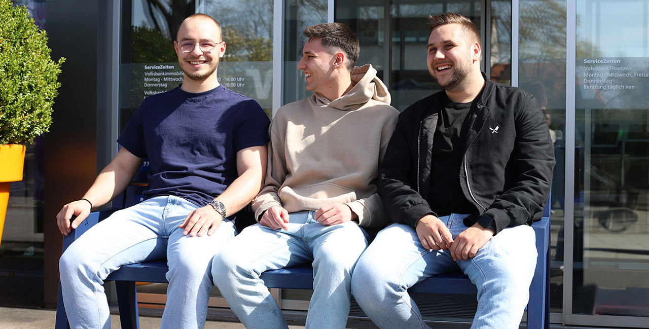 Drei junge Männer sitzen lächelnd auf einer Bank
